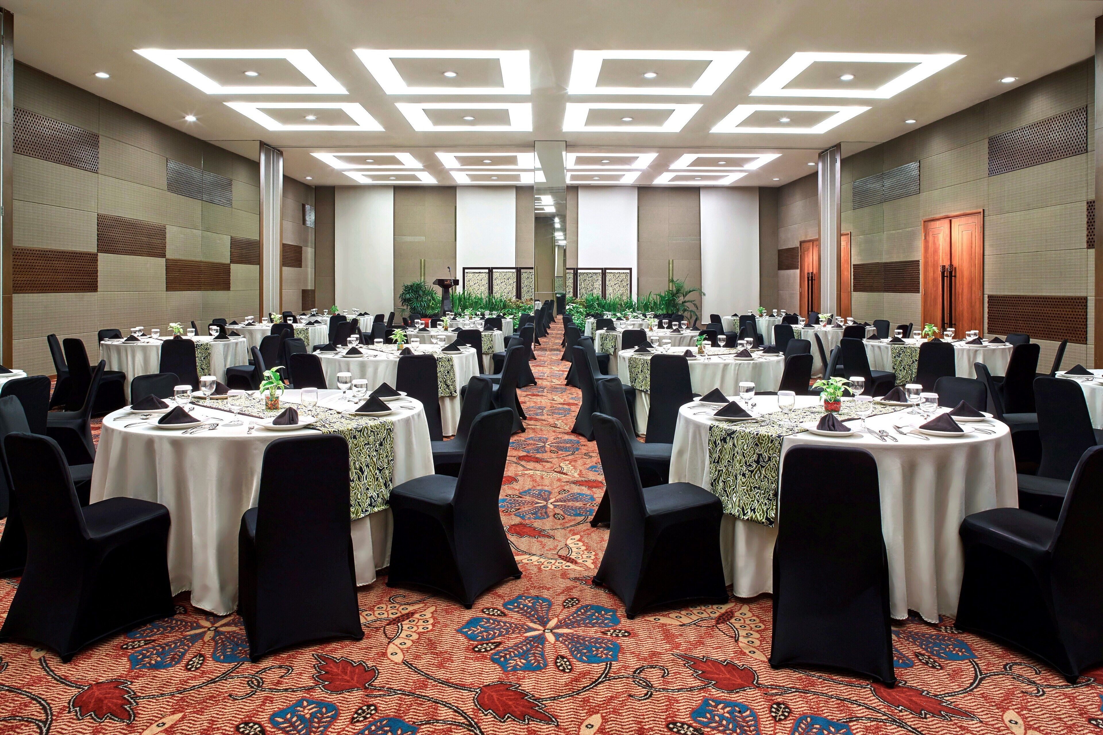 A banquet hall with round tables, black chairs, and a patterned carpet.