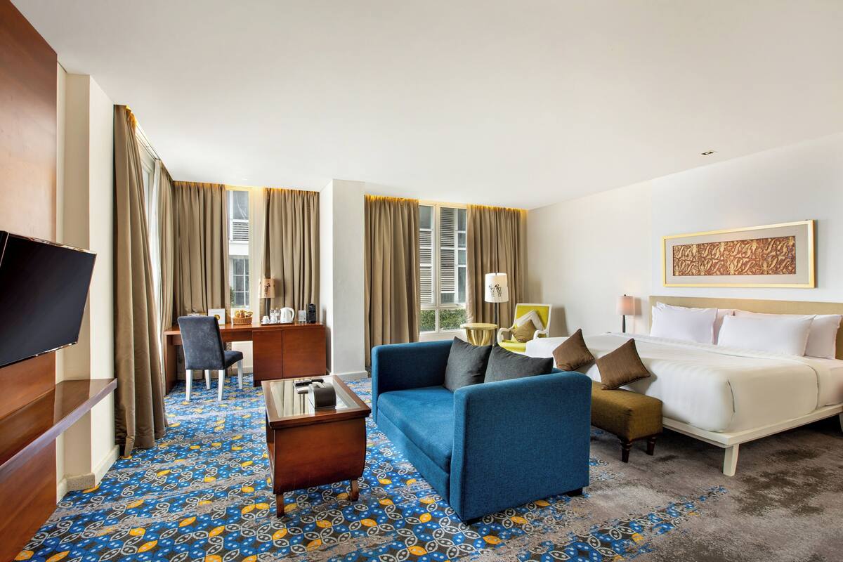 Une chambre d’hôtel avec un lit, un canapé bleu, un bureau avec une chaise, une télévision et une moquette à motifs.