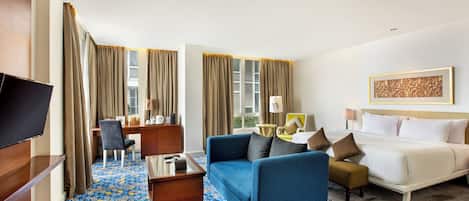 Habitación de hotel con cama, sofá azul, escritorio con silla, televisor y alfombra estampada.