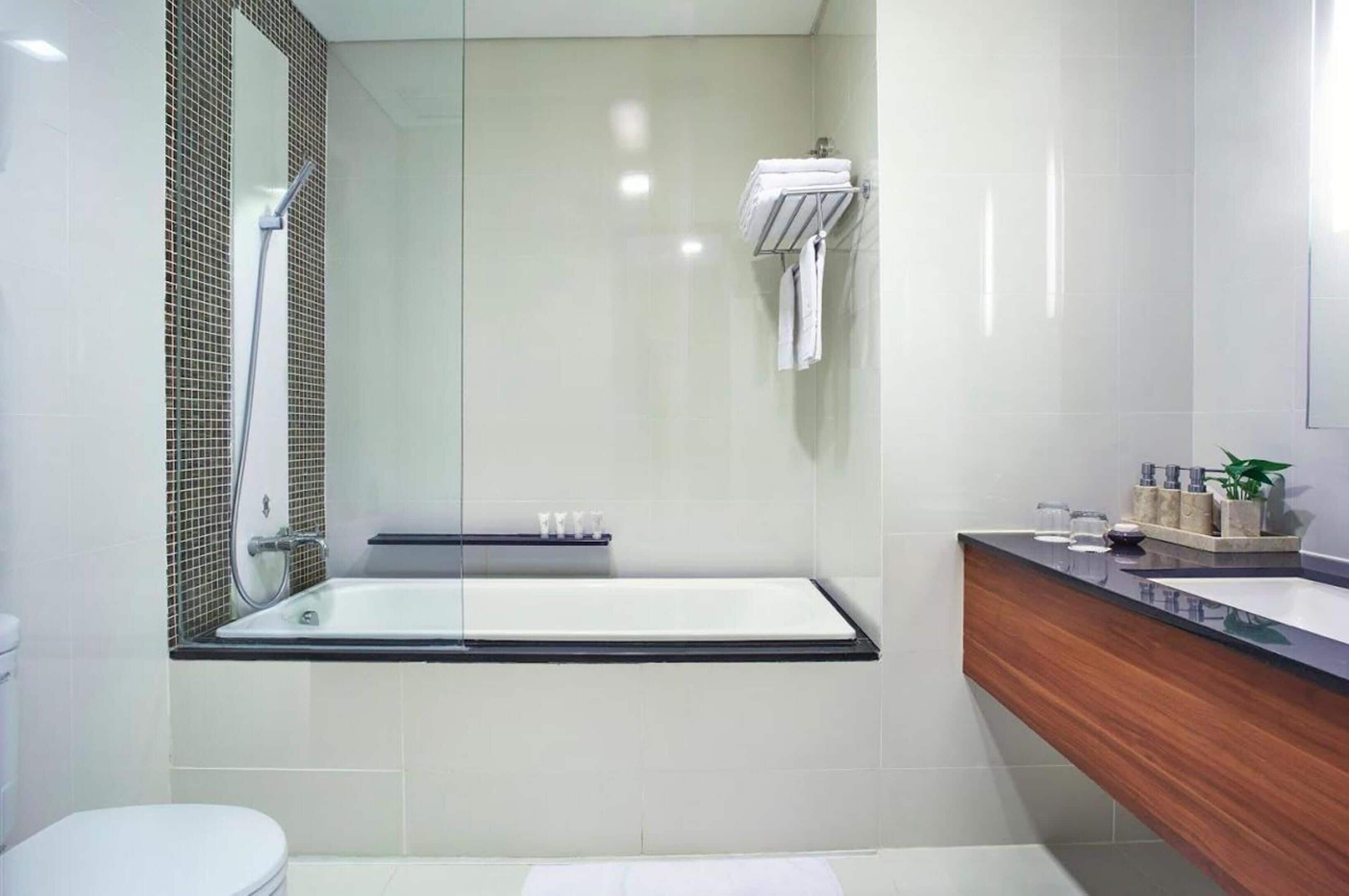 Un baño moderno con ducha de vidrio, una bañera independiente y un tocador de madera con lavamanos.