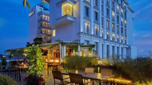 A modern hotel with a well-lit outdoor patio area, featuring tables and chairs, and a large building with multiple windows.