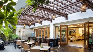 An outdoor dining area with wooden tables and chairs, a pool, and a covered patio with a wooden ceiling.