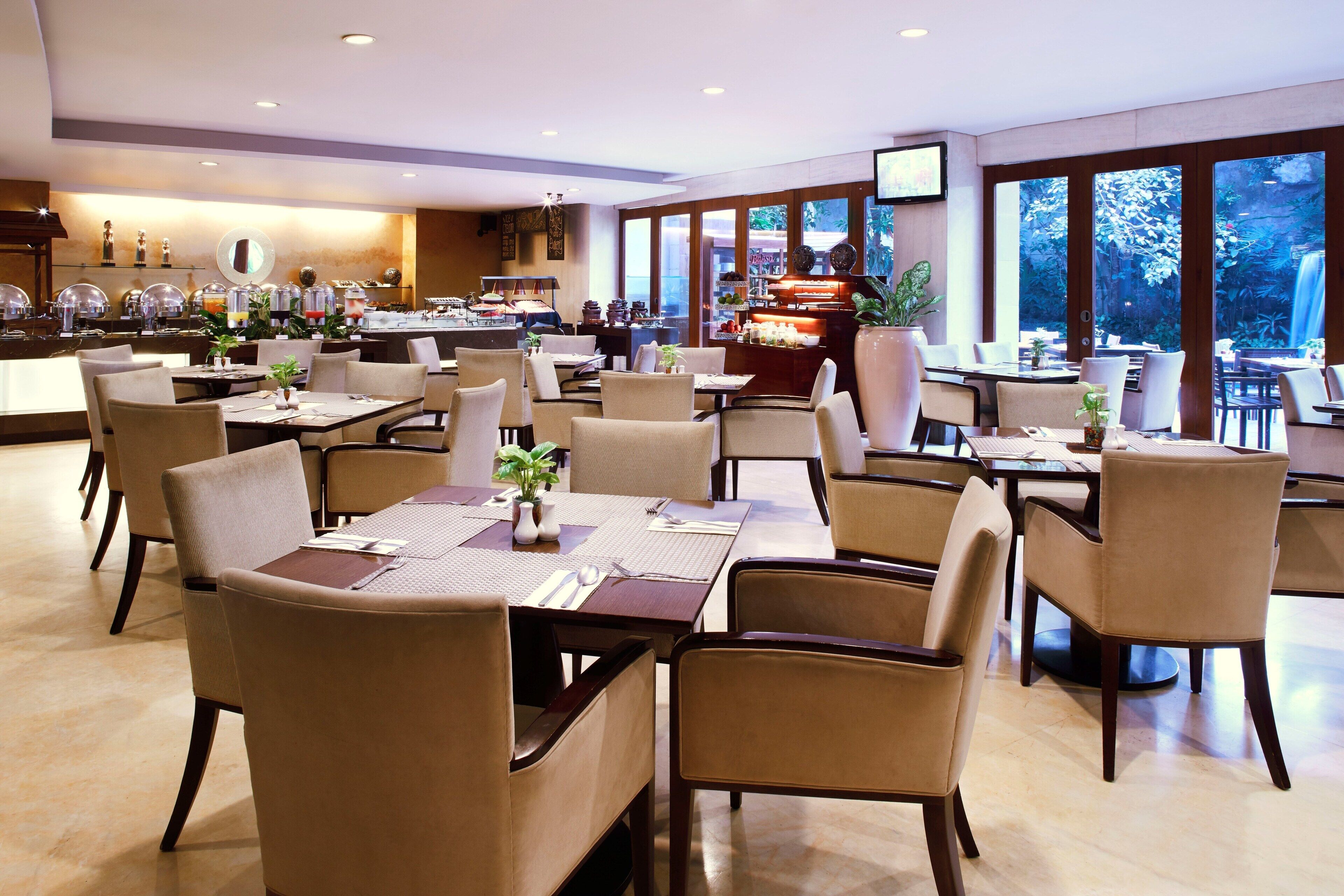 Een ruim restaurant met meerdere tafels en stoelen, een buffetgedeelte en grote ramen met uitzicht op het landschap.