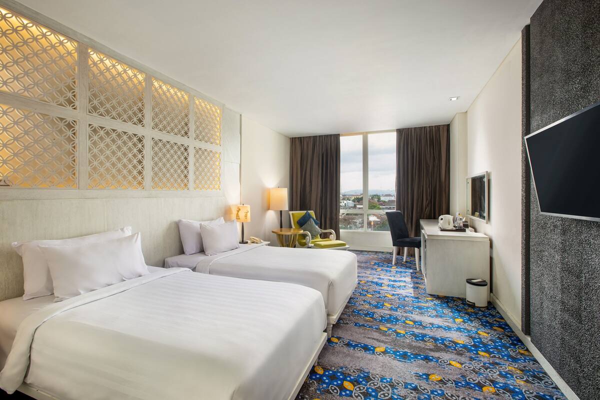 Une chambre d’hôtel avec deux lits, un bureau, une chaise, une télévision et une grande fenêtre donnant sur un beau paysage.