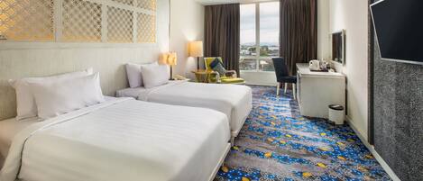 A hotel room with two beds, a desk, a chair, a TV, and a large window with a view.