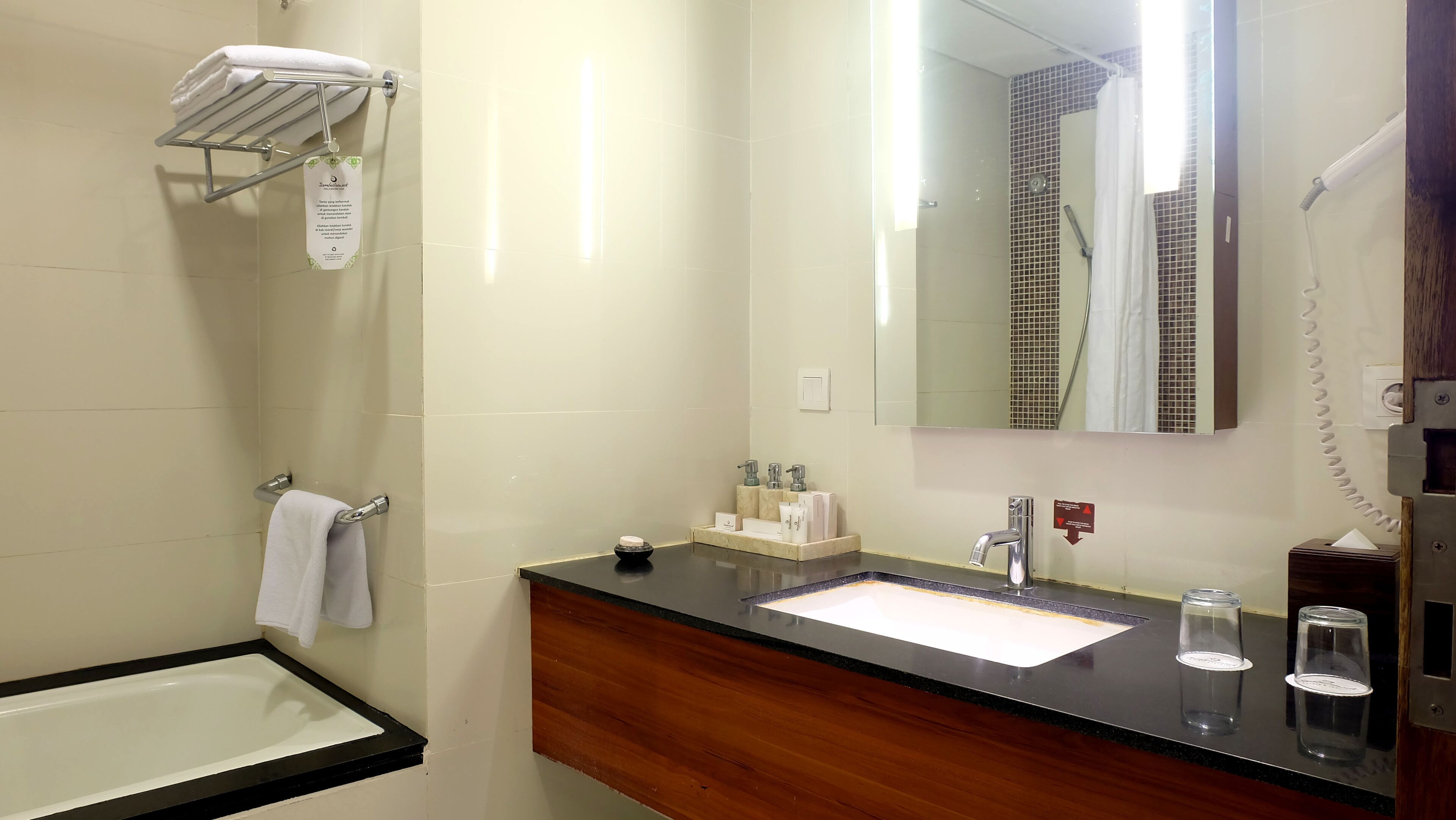 Un baño con una bañera, un lavabo con encimera de mármol, un espejo y un perchero con una toalla doblada.