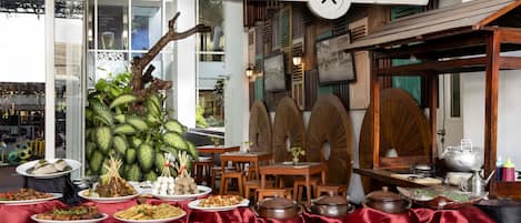 Interior de un restaurante con varios platos exhibidos, muebles de madera y un letrero que dice 'Mbok Luwuk'.