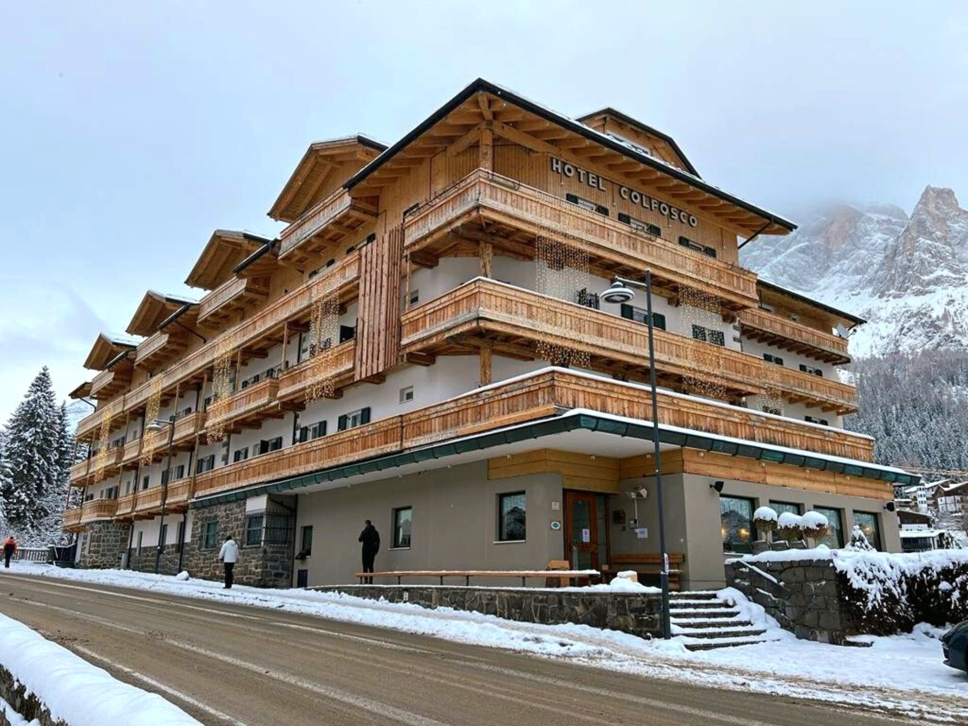 A multi-story hotel with wooden balconies and a sign reading "Hotel Colfosco".