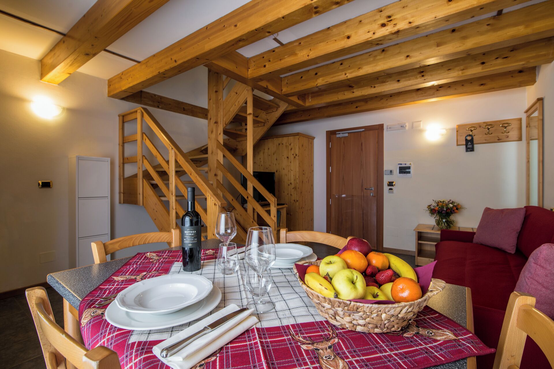 Ein Essbereich mit Holzbalkendecke, einer Treppe, einem Kühlschrank und einer Obstschale auf dem Tisch.