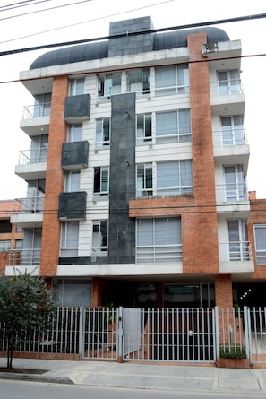 A multi-story building with a mix of brick and concrete facades, balconies, and a gated entrance.