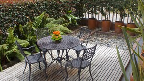 Una mesa redonda de metal con cuatro sillas, rodeada de plantas en macetas y una terraza de madera.