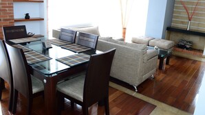 Una sala de estar moderna con una mesa de comedor de vidrio, sillas de madera, un sofá gris y una chimenea.