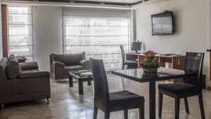 Una sala moderna con una mesa de centro de vidrio, un sofá, una mesa de comedor con sillas y un televisor montado en la pared.
