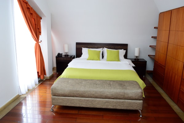 A neatly made bed with a green and white bedspread, two bedside tables with lamps, and a wooden wardrobe.