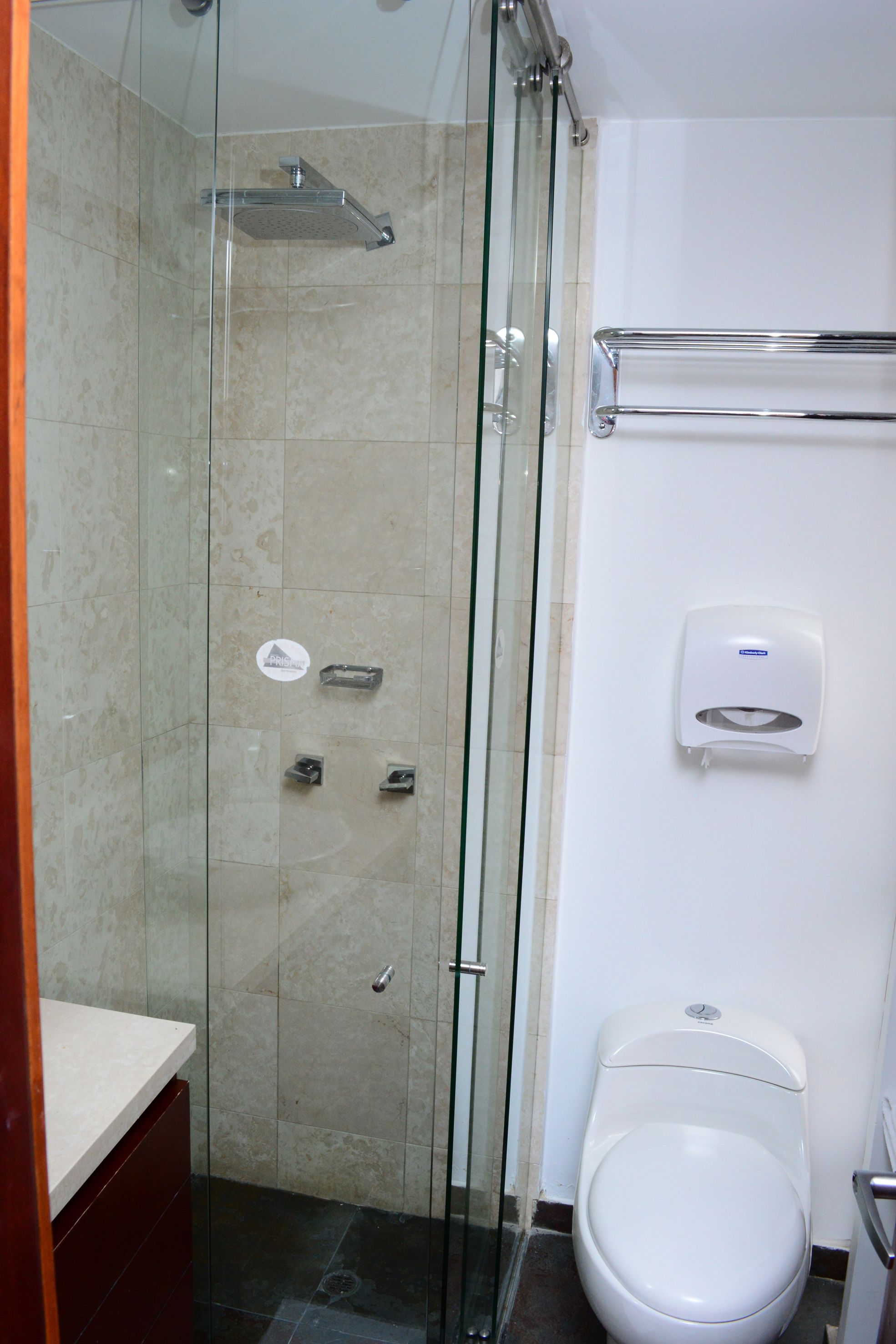 Un baño con cabina de ducha de vidrio, inodoro y secador de manos.