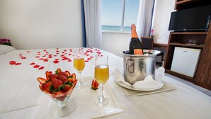 A neatly made bed with a bouquet of flowers, a champagne bottle, and a bowl of strawberries. - Praia Linda (Rio de Janeiro)