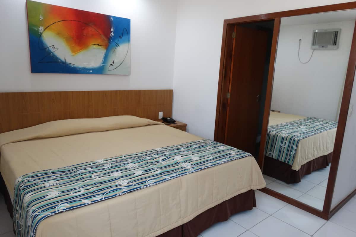 A hotel room with a bed, a nightstand, a mirror, and a colorful abstract painting on the wall.