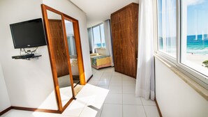 A hotel room with a TV, a large mirror, a bed, a wardrobe, and a view of the ocean. - Praia Linda (Rio de Janeiro)