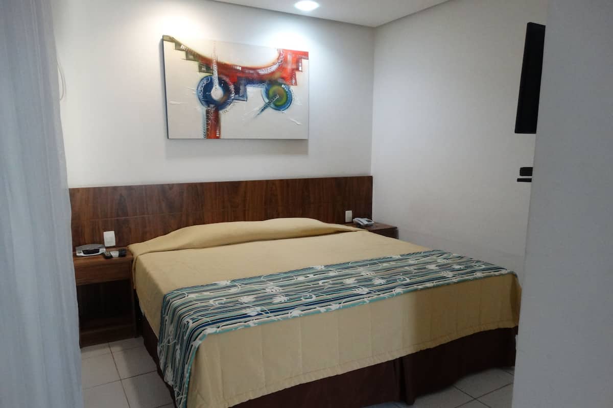 A hotel room with a bed, a nightstand, a telephone, and a wall-mounted abstract painting.
