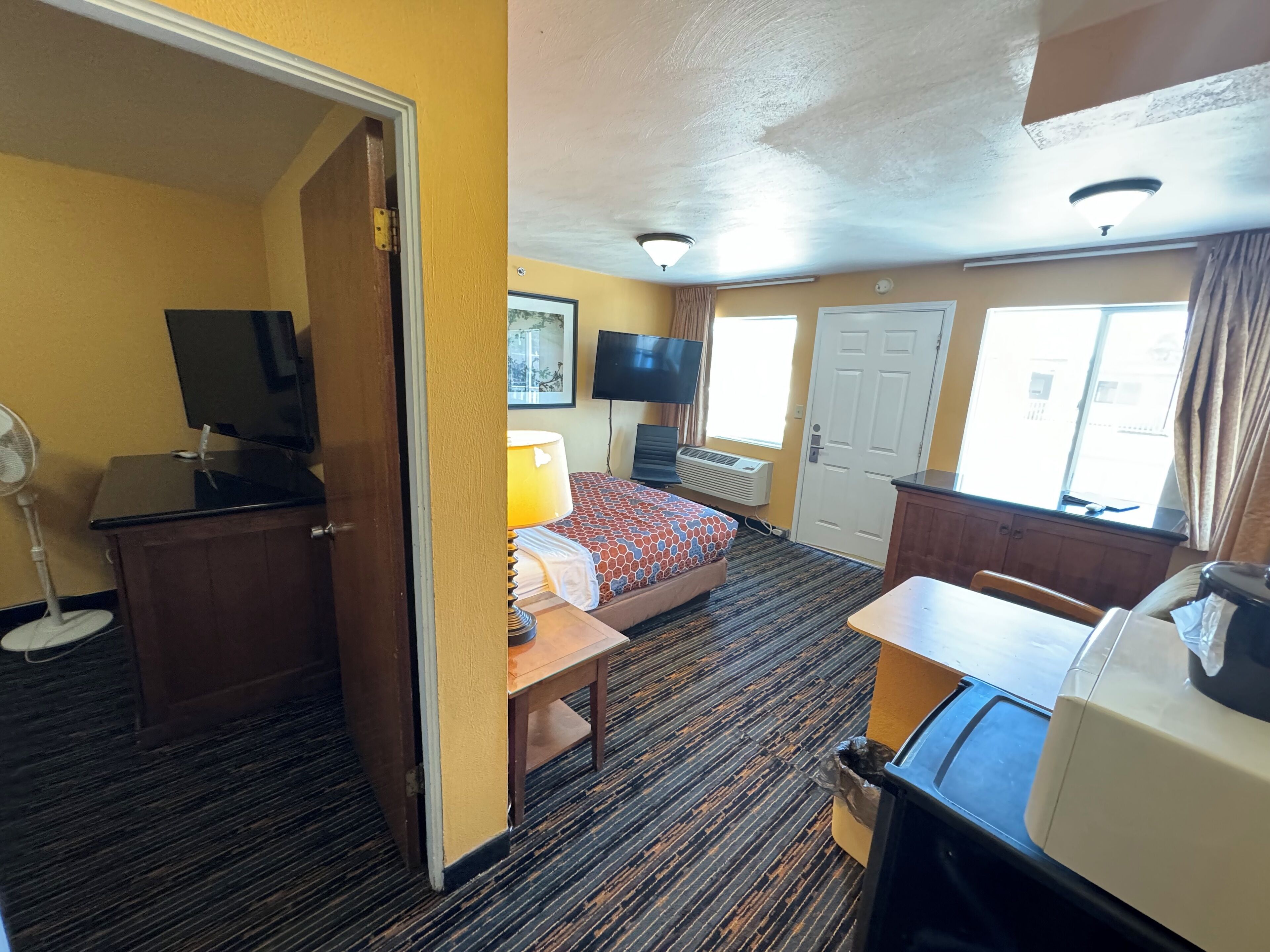 A hotel room with a bed, desk, TV, and a small table.