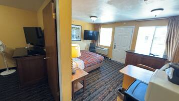A hotel room with a bed, desk, TV, and a small table.