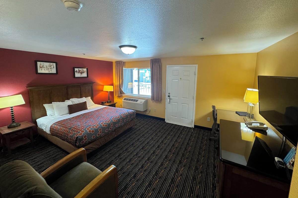 A hotel room with a bed, a desk, a chair, a TV, a window with curtains, and an air conditioning unit.
