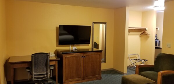 Una habitación de hotel con un escritorio de madera, una silla, un televisor, un espejo y un perchero.