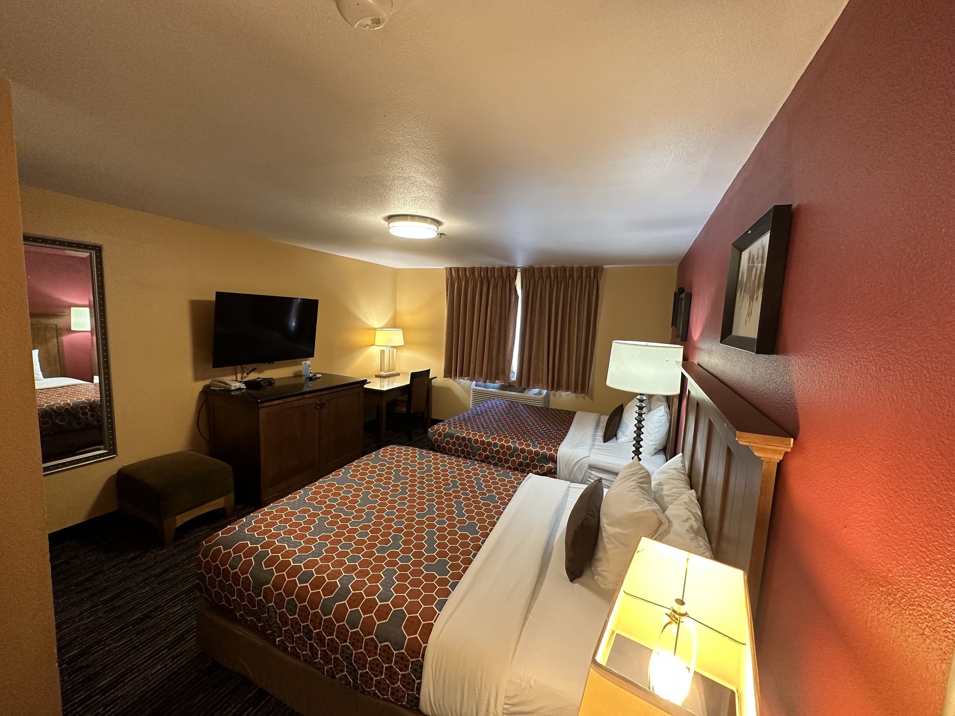 Une chambre d’hôtel avec deux lits, un bureau, une télévision et une fenêtre avec des rideaux.