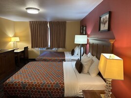 Una habitación de hotel con cama, escritorio, silla, lámpara y ventana con cortinas.