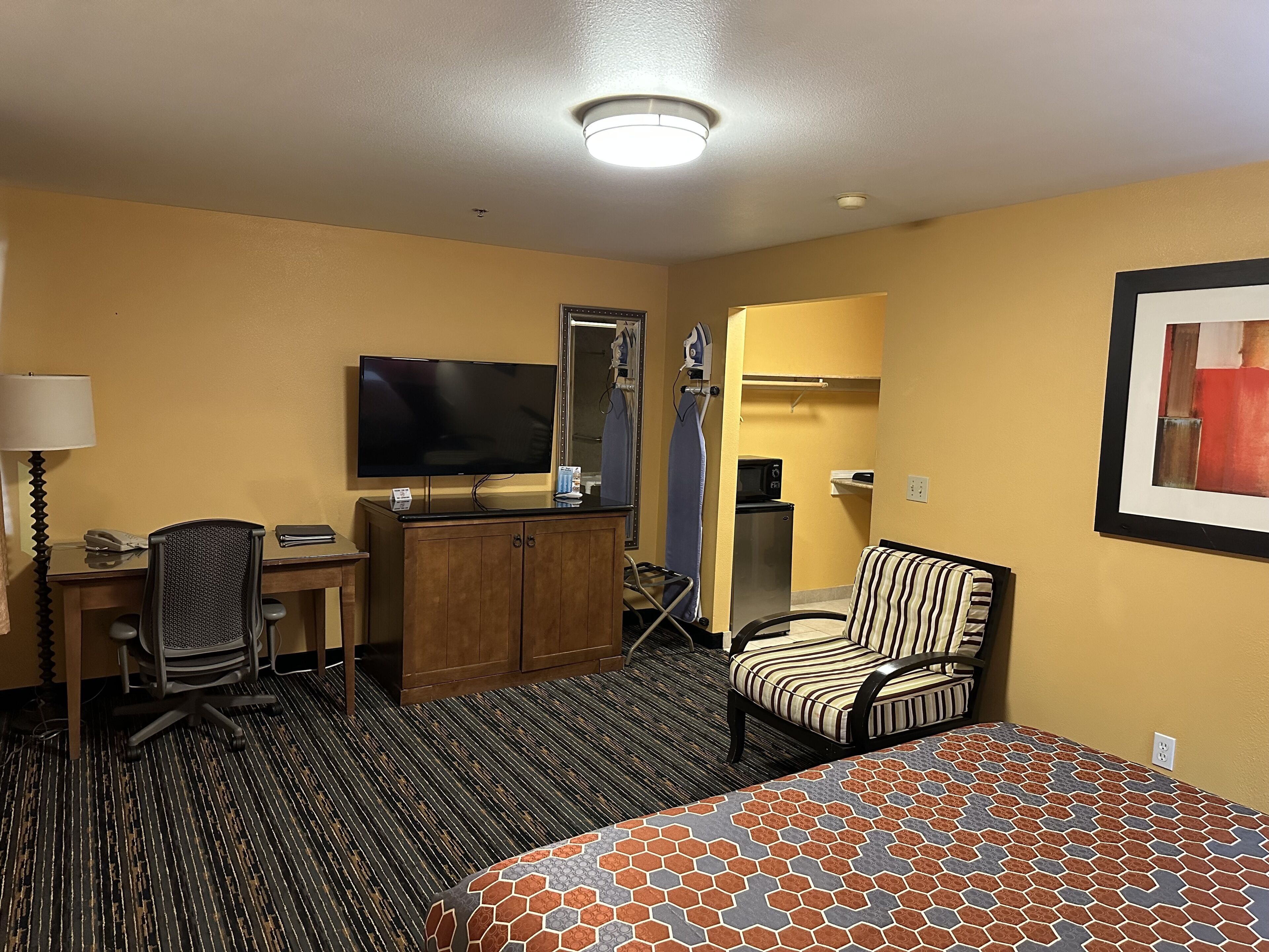 Une chambre d’hôtel équipée d’un lit, d’un bureau avec une télévision, d’une chaise, d’une armoire et d’un four à micro-ondes.