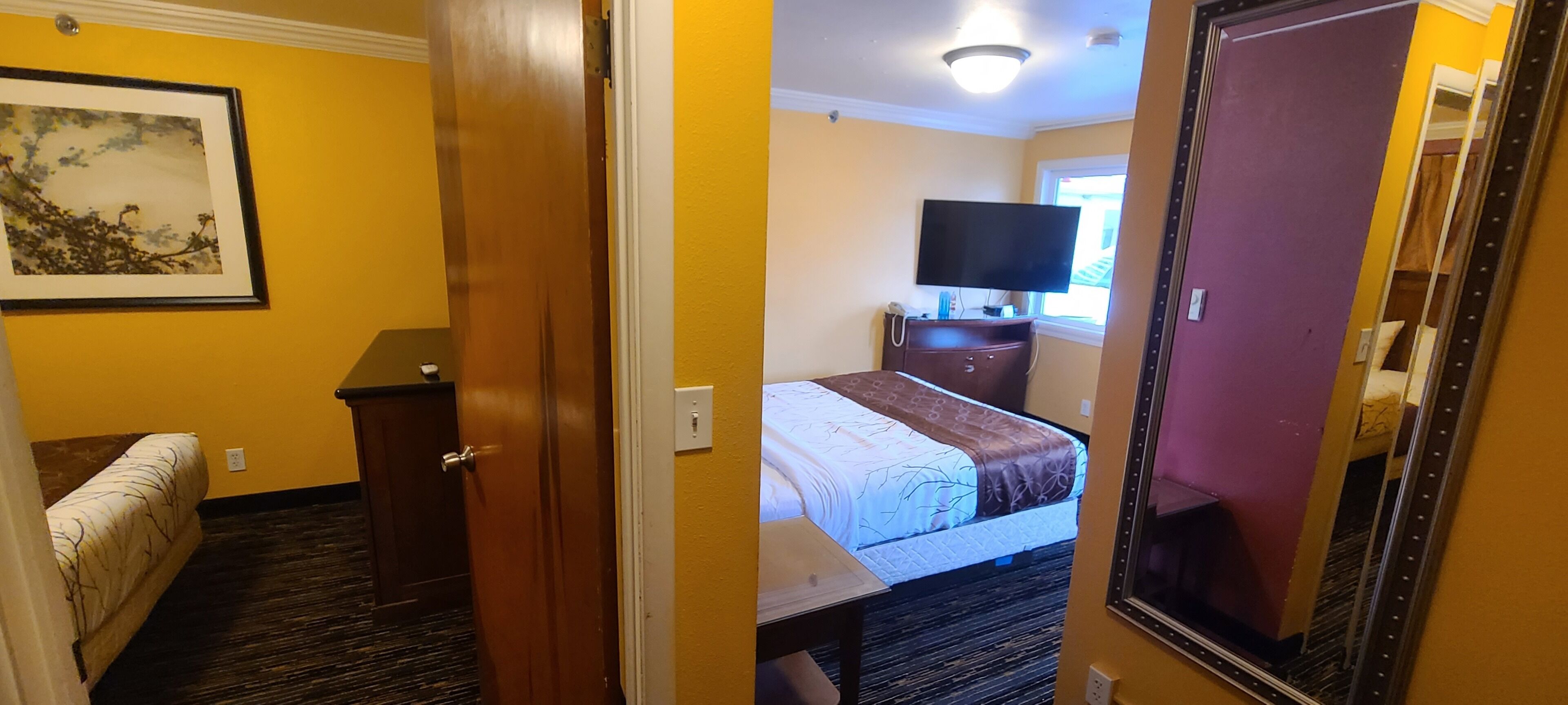 A hotel room with a bed, a desk, a dresser, a television, and a window.