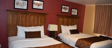 A hotel room with two beds, wooden headboards, white linens, brown throw blankets, and framed artwork on the walls.
