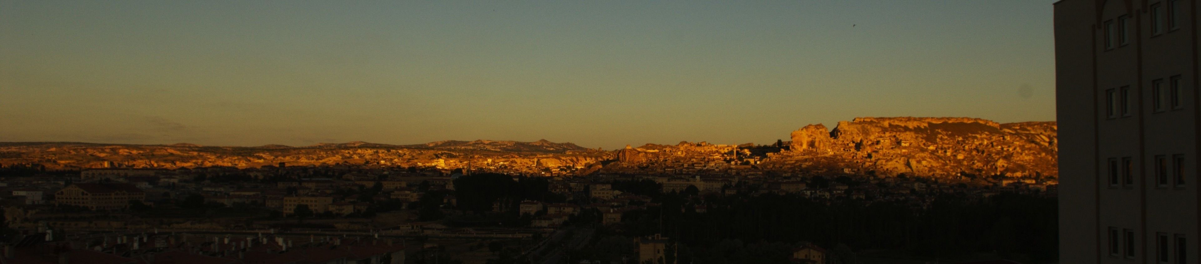 Un paisaje urbano al atardecer con una colina o montaña destacada en el fondo.