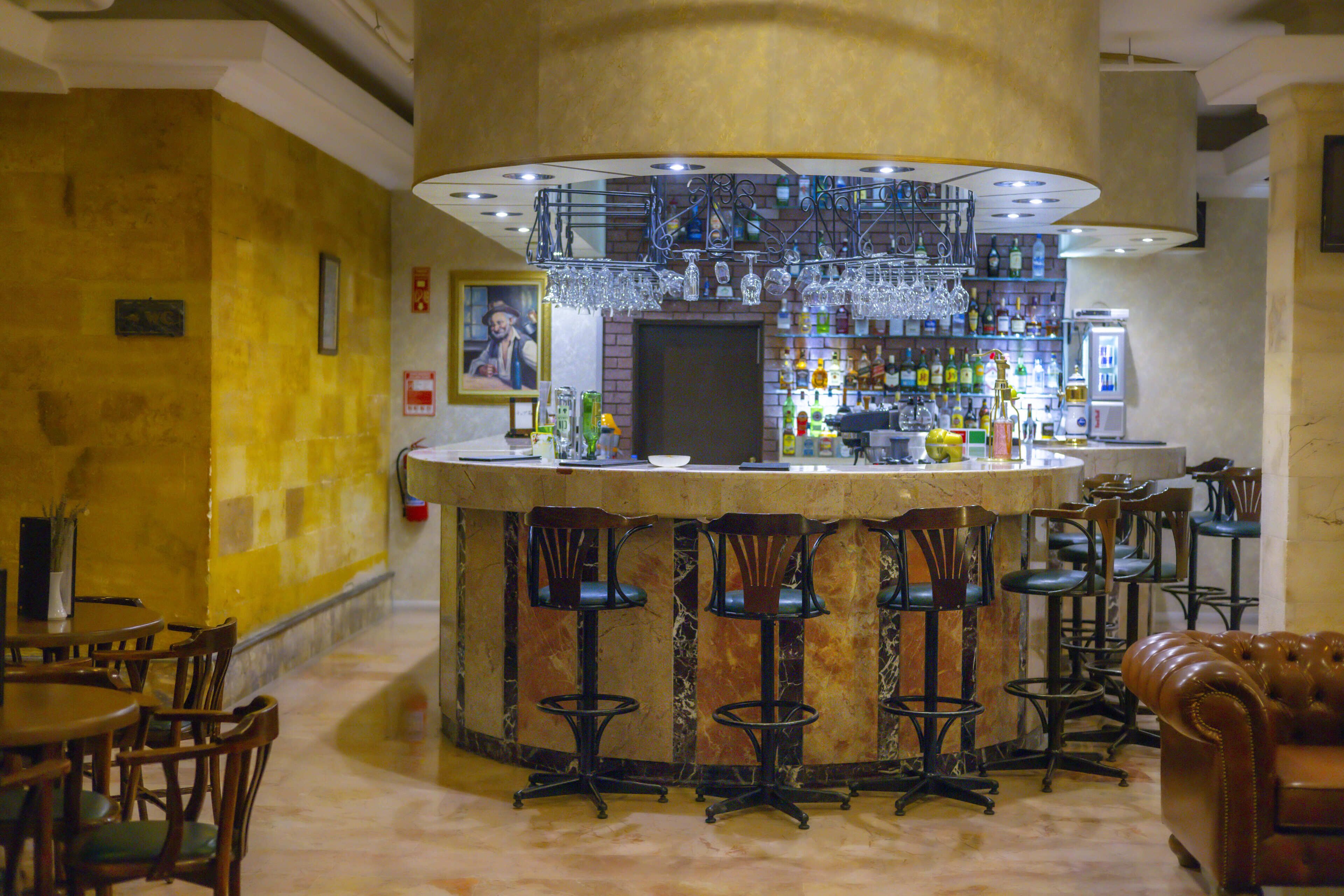 A bar area with a marble counter, multiple stools, and a variety of bottles and glasses.