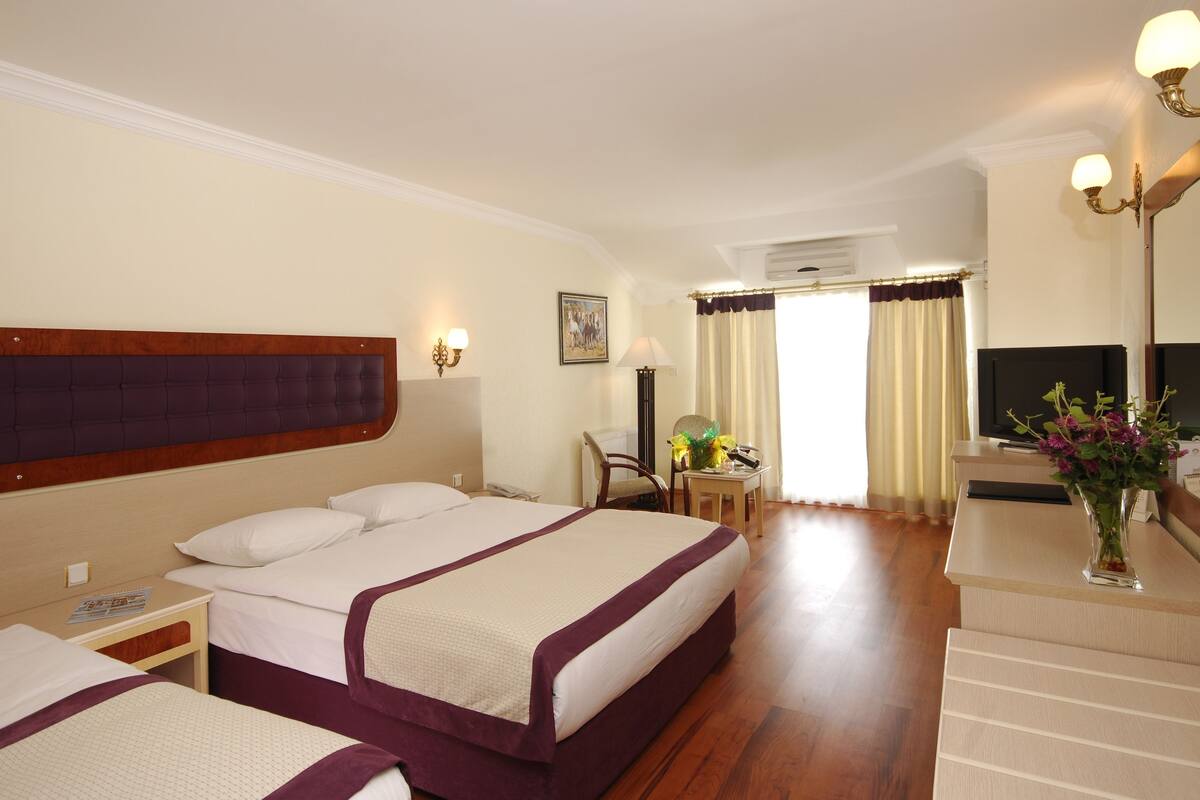 Ein Hotelzimmer mit zwei Betten, einem Schreibtisch, einem Stuhl, einem Fernseher und einem Fenster mit Vorhängen.