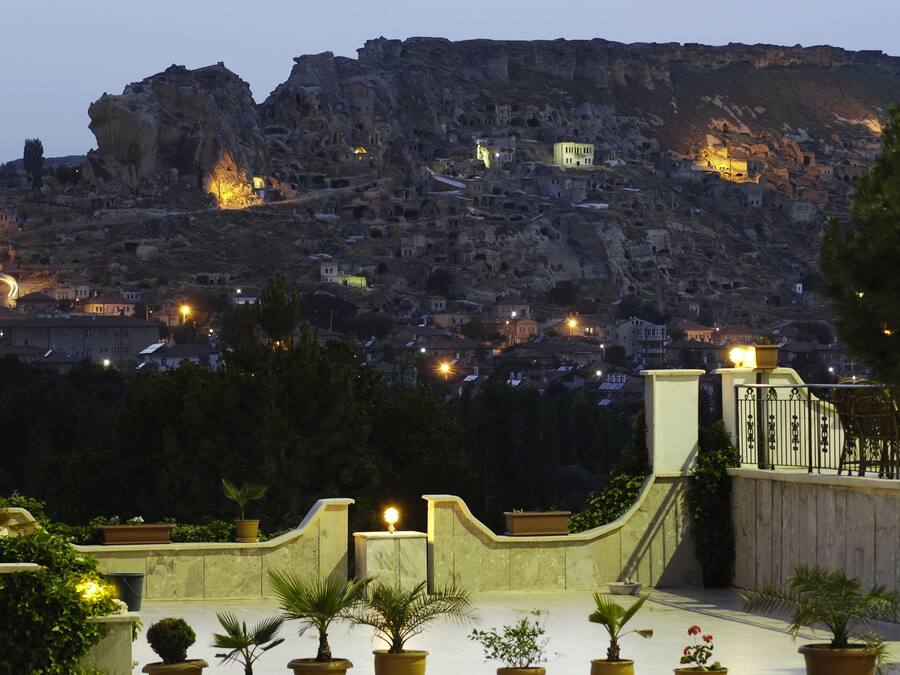 Vista de un pueblo con edificios ubicados en una ladera rocosa, un balcón con plantas en macetas y una barandilla.