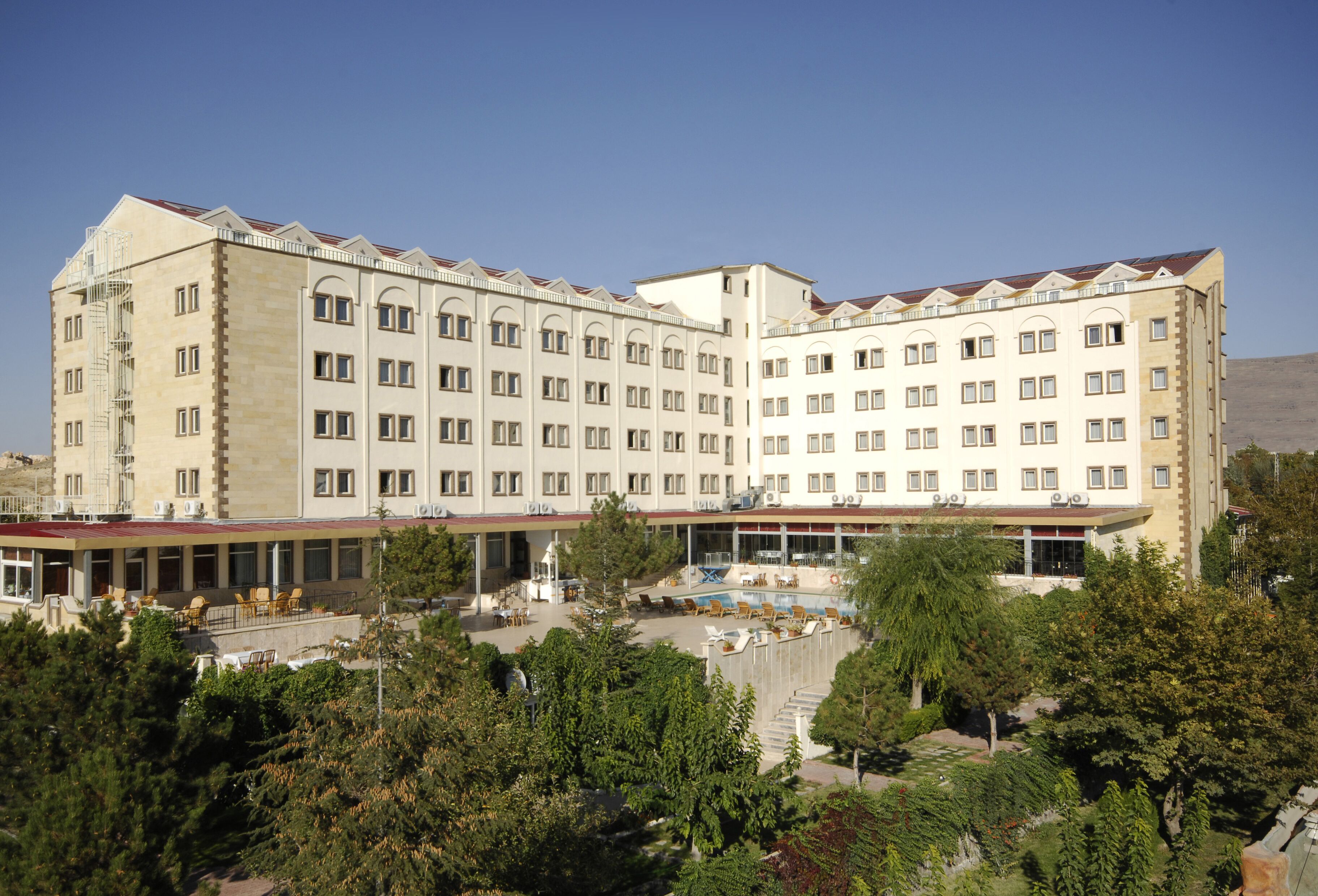 Un hotel grande de varios pisos con un patio central, rodeado de árboles y una piscina.