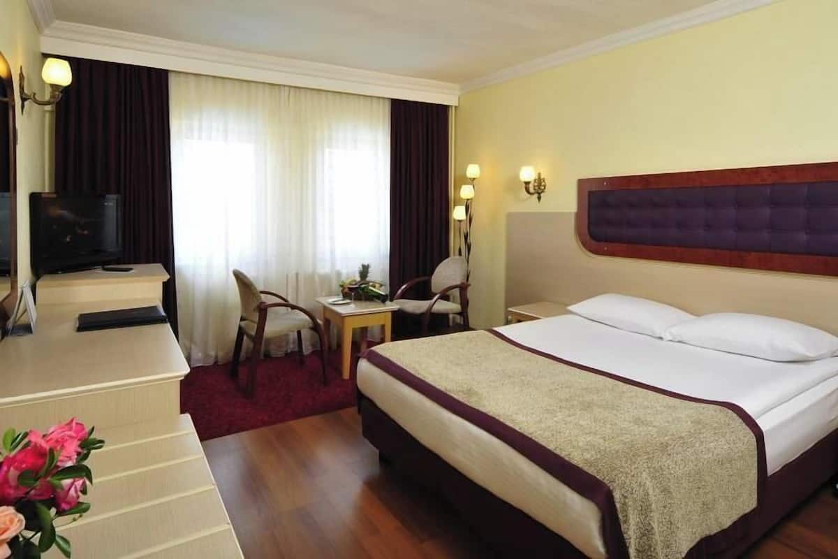 Ein Hotelzimmer mit einem Bett, einem Schreibtisch, einem Stuhl, einem Fernseher und einem Vorhangfenster.