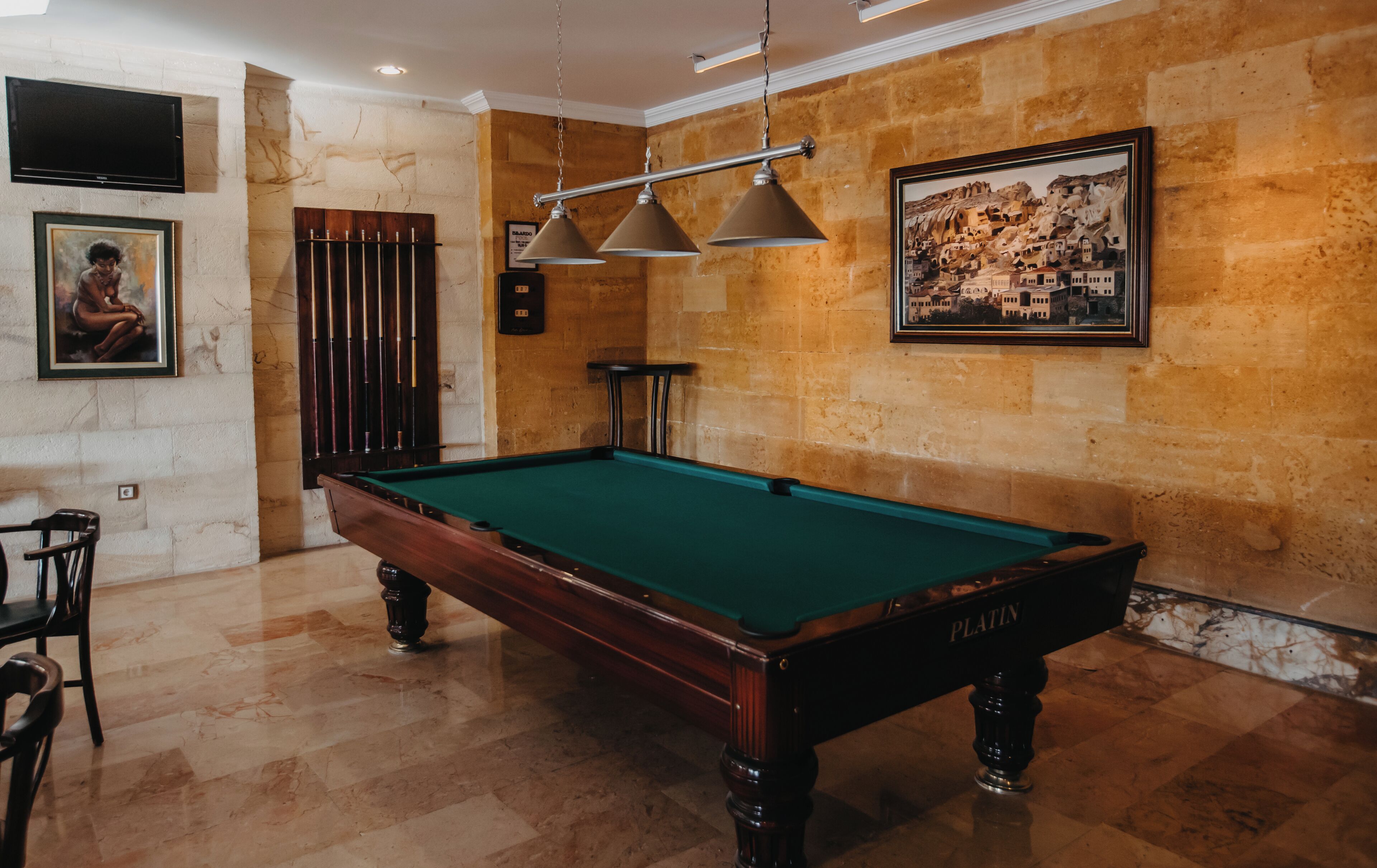 A billiards table in a room with a stone wall, a mounted television, and framed artwork.