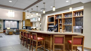 A bar area with wooden bar stools, a countertop with a coffee machine, and shelves stocked with bottles.