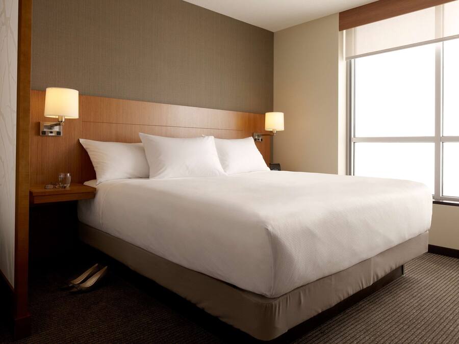Una habitación de hotel con una cama grande, dos lámparas de noche, un cabecero de madera y un ventanal amplio.