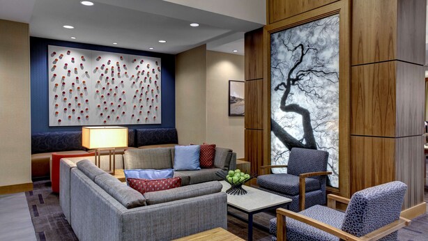 A modern hotel lobby with a sofa, armchairs, a coffee table, and a large abstract painting.