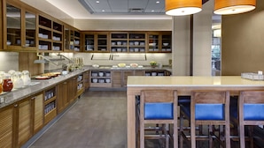 A modern kitchen with wooden cabinets, a central island with bar stools, and a variety of bowls and utensils on the counter.