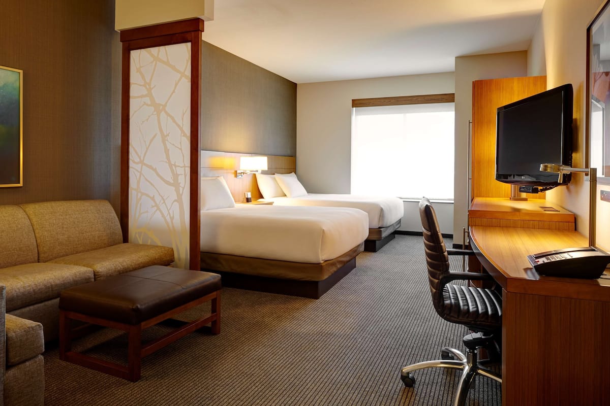 A hotel room with two beds, a sofa, a desk with a computer, and a TV.