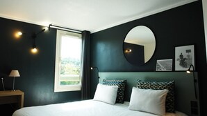 Quarto de hotel moderno com uma cama grande, um espelho redondo e vista para o verde lá fora.
