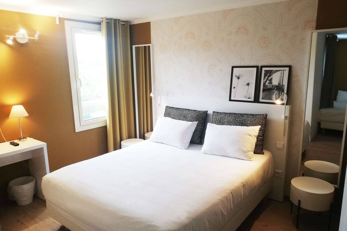 Ein ordentlich eingerichtetes Hotelzimmer mit einem großen Bett, Nachttischen, einem Schreibtisch und einem Fenster mit Vorhängen.