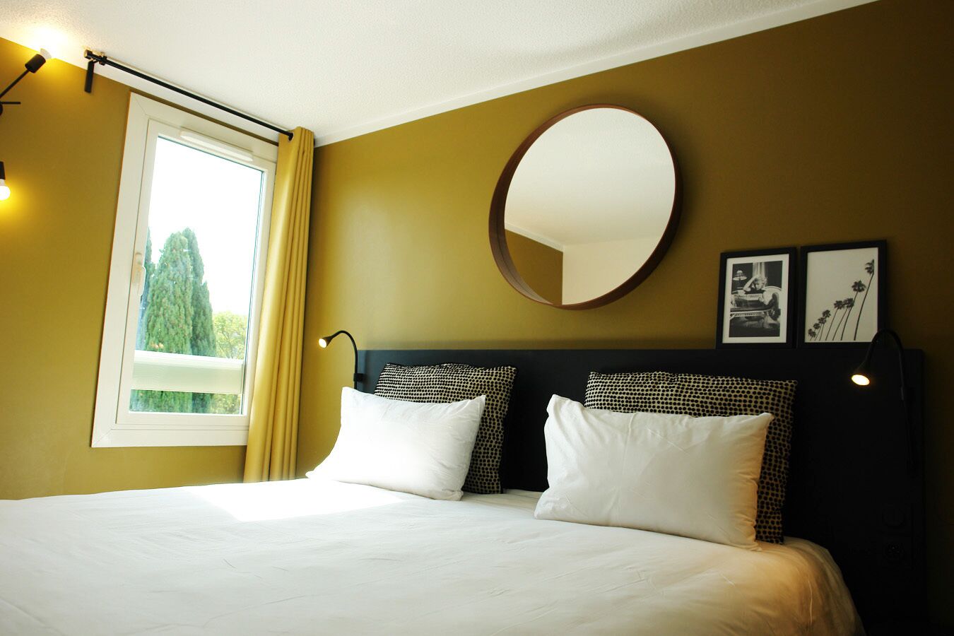 A hotel room with a large bed, a round mirror, and two framed pictures on the wall.