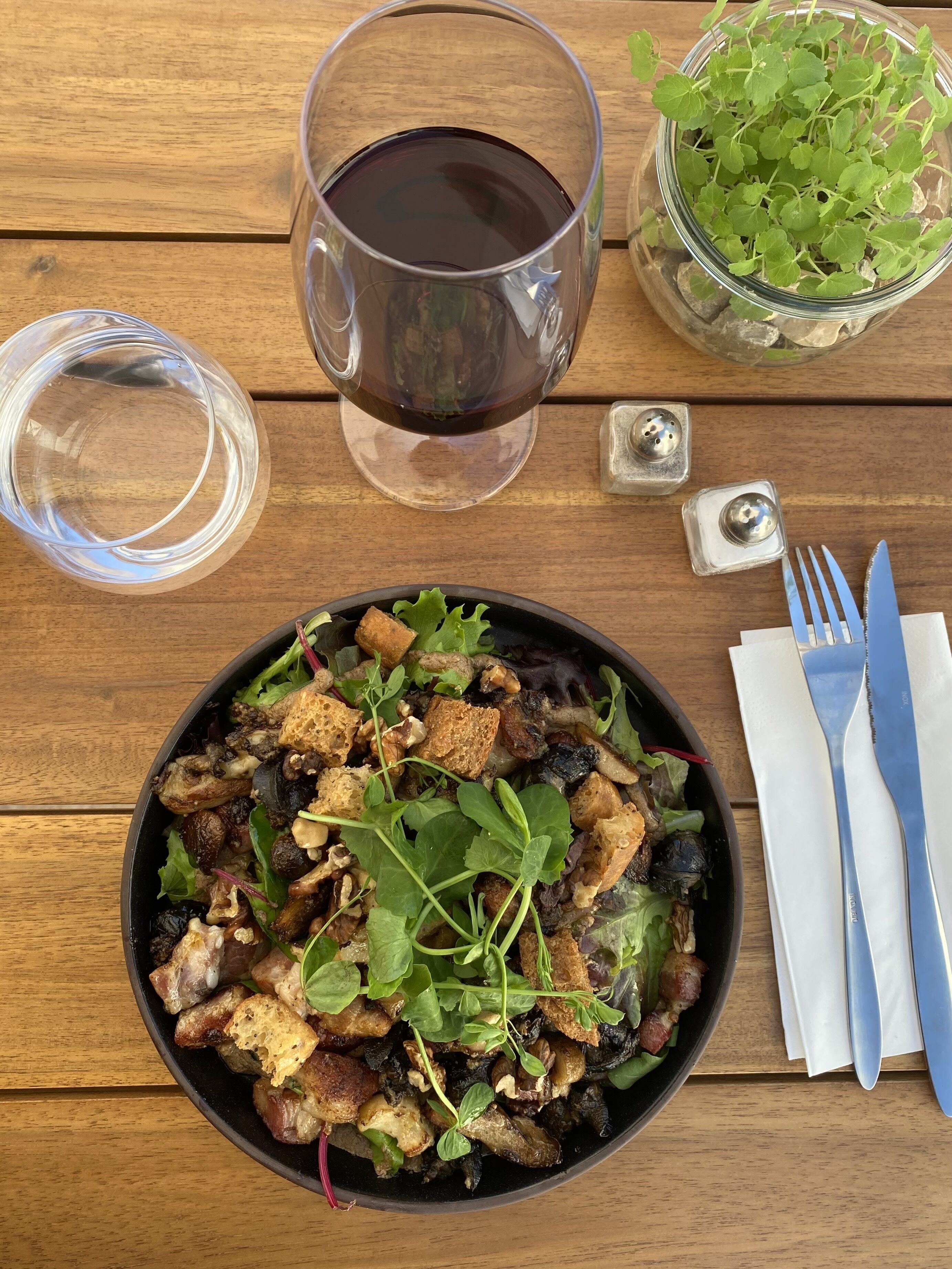Una comida con ensalada, una copa de vino tinto y un vaso de agua sobre una mesa de madera.