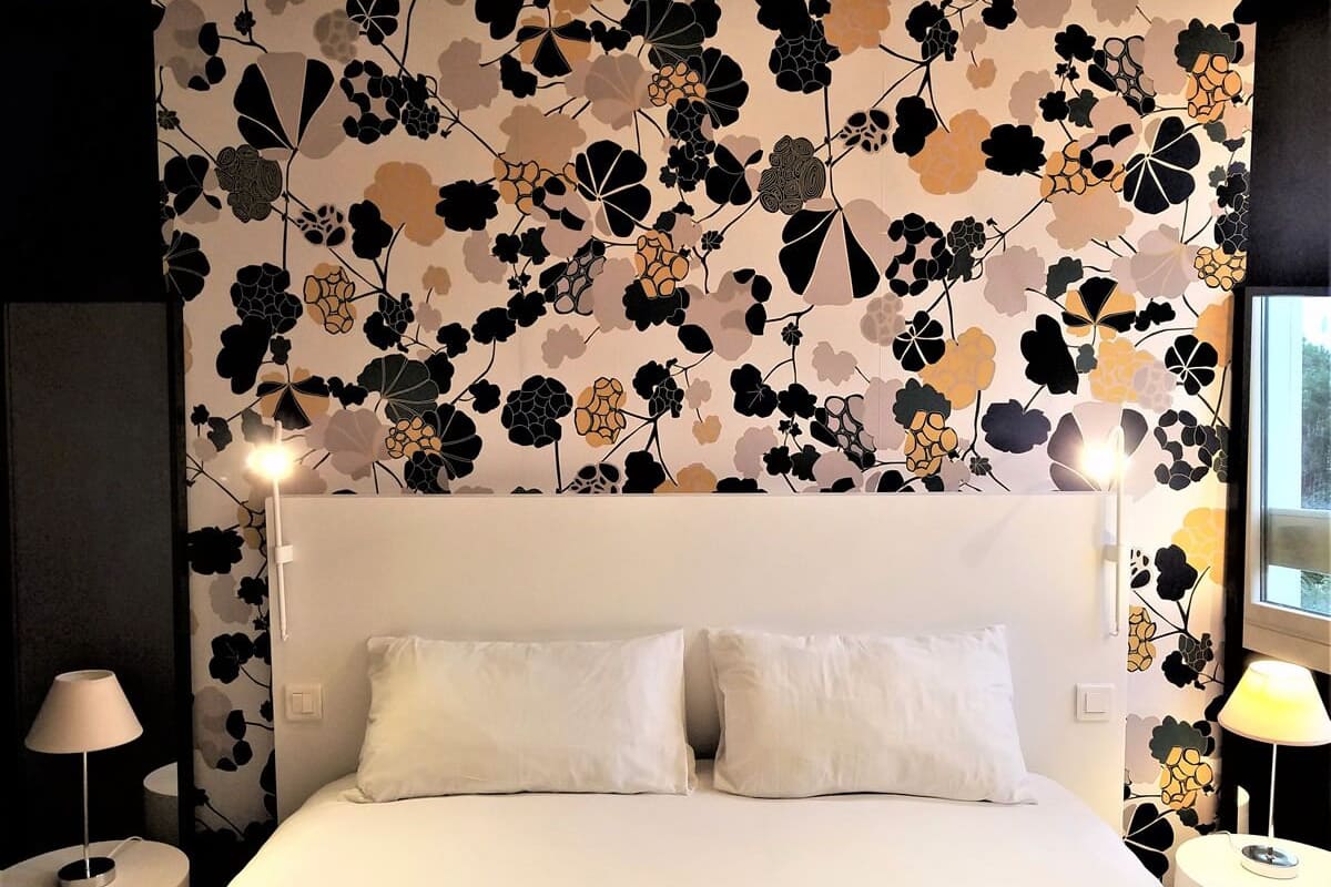 Ein Hotelzimmer mit einem großen Bett, zwei Nachttischlampen und einem blumigen Wanddesign.