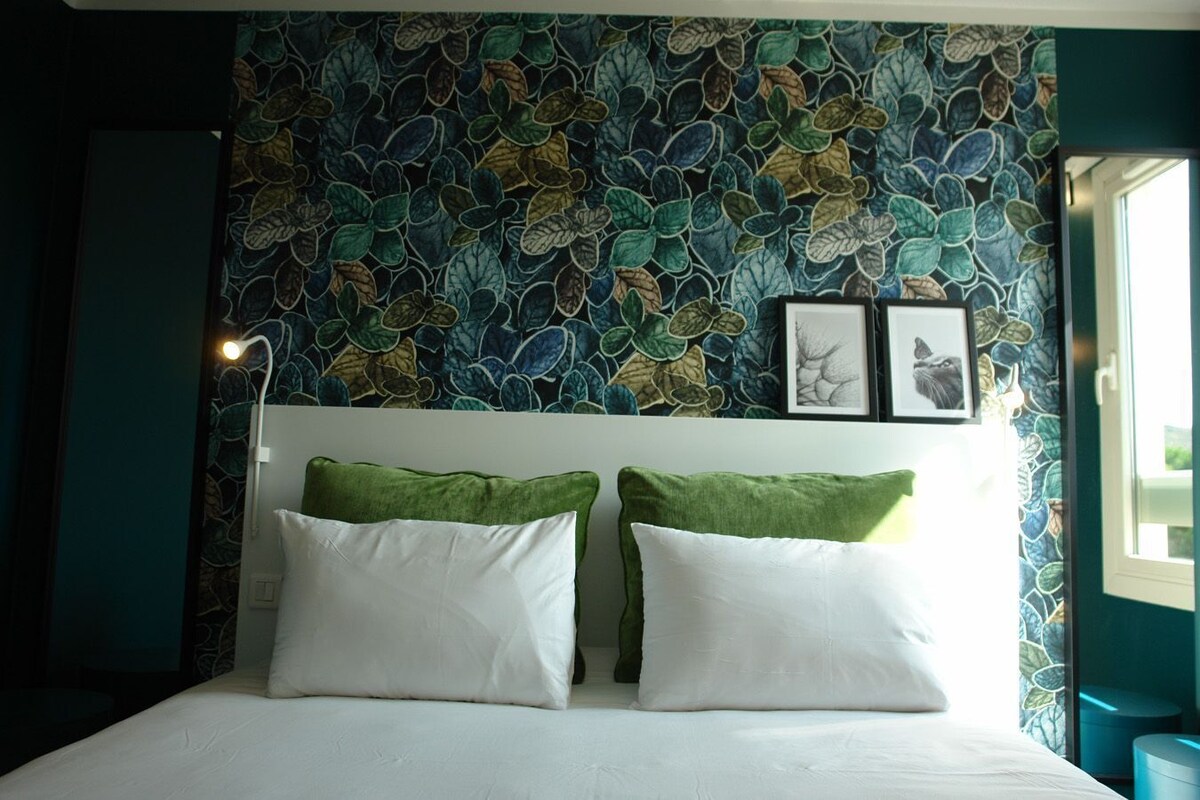 A bedroom with a bed, two pillows, a headboard, and a wall with a leafy pattern.